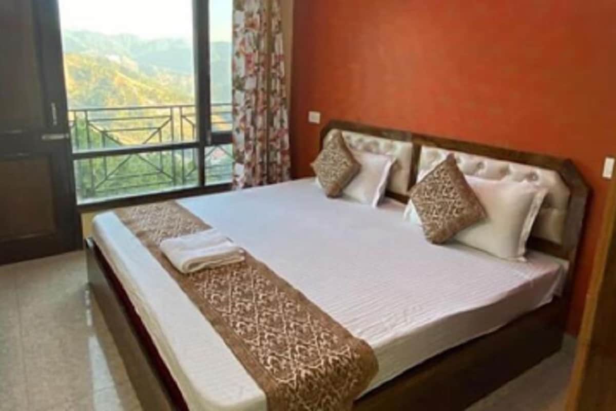 A bedroom with a large bed, a view of mountains through a balcony, and a wooden headboard.