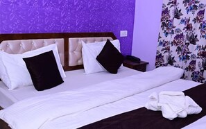 A hotel room with a large bed, two black and white pillows, a wooden headboard, a nightstand with a phone, and a floral curtain. - Eden Hotel & Resort Shimla (Shimla)