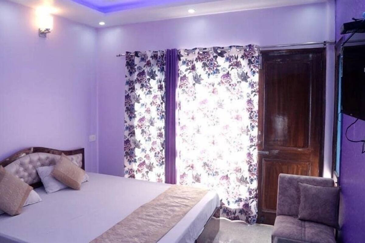 A bedroom with a bed, a chair, a window with floral curtains, and a wooden door.