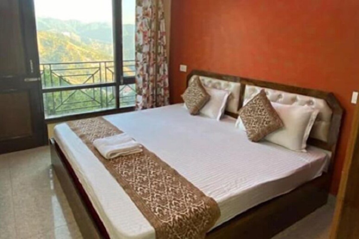 A bedroom with a large bed, a view of mountains through a balcony, and a wooden headboard.