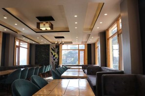 Un restaurant moderne avec de longues tables et des chaises vertes, de grandes fenêtres et un mur décoratif.