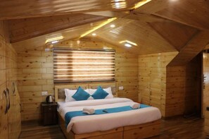 A wooden cabin room with a bed, a nightstand, and a window with blinds. - Eden Hotel & Resort Shimla (Shimla)