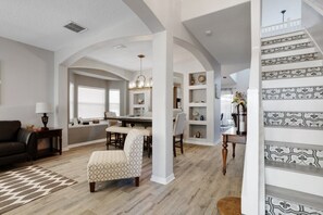A spacious living area with a dining table, a sofa, and a patterned rug. - Six Bedroom Disney Home Lanai, SouthEast facing Screened Pool & Spa only a few mins to Disney (Kissimmee)