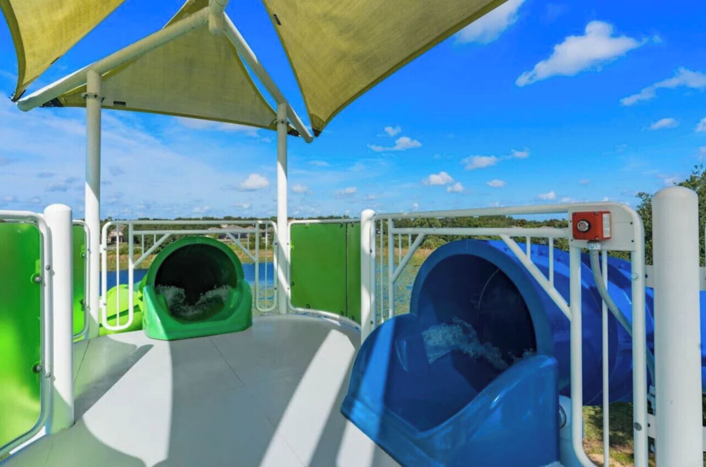 A water slide with green and blue slides, surrounded by safety railings and a canopy.