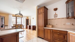 Een ruime keuken met houten kasten, een eetgedeelte met een kroonluchter, en uitzicht op de eetkamer.