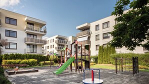 Een buitenspeelplaats met glijbanen en klimconstructies, omgeven door appartementencomplexen.