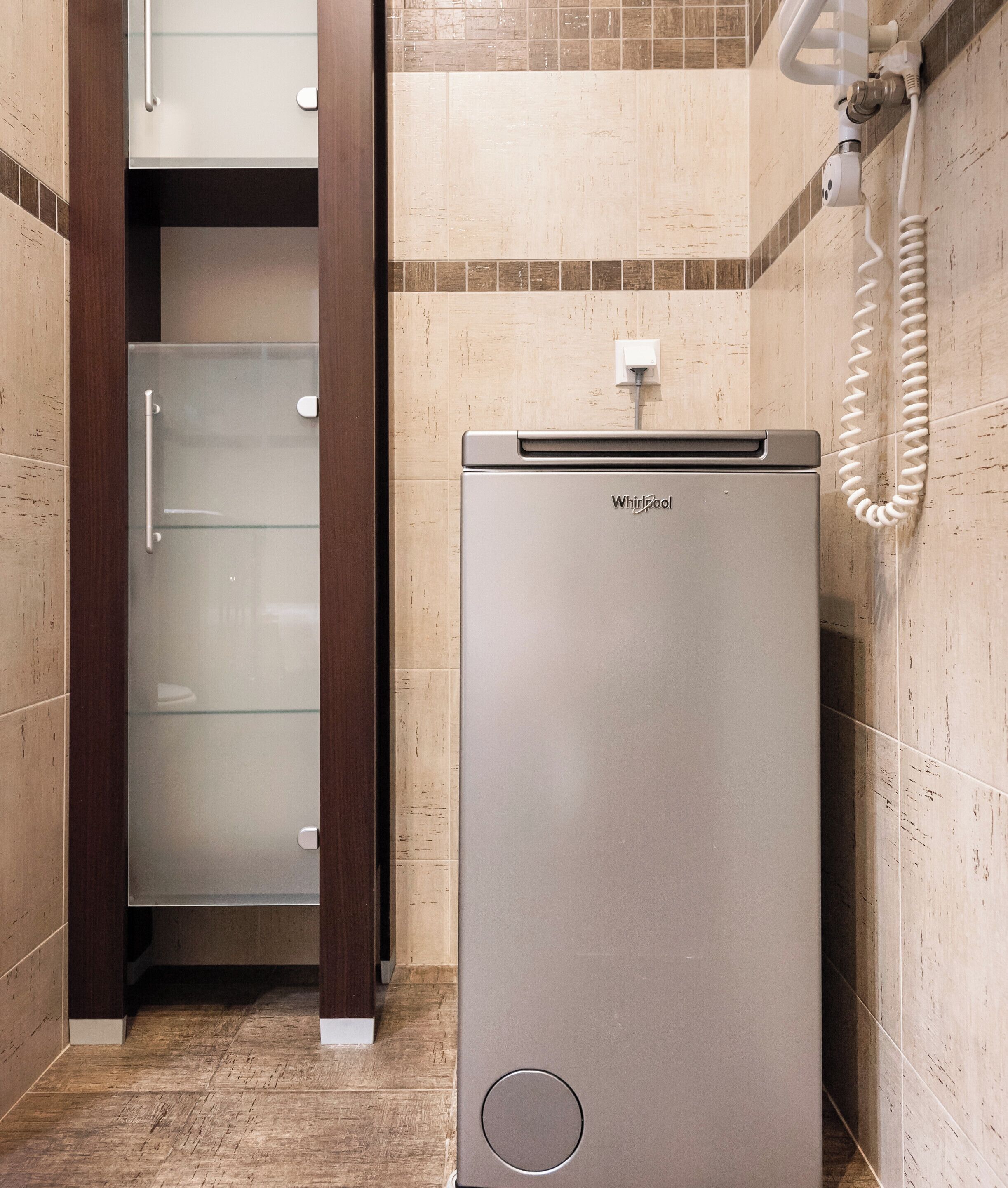 Un baño moderno y funcional con un refrigerador Whirlpool integrado, cerramiento de ducha de vidrio y un secador de pelo de pared.