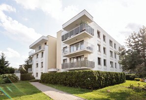 Un immeuble résidentiel moderne à plusieurs étages, doté de balcons, d’un chemin pavé et d’un espace vert bien entretenu.