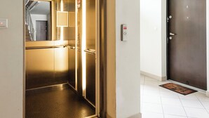 Een lift met een metalen interieur, een zichtbaar bord met daarop een nooduitgang en een deur met het nummer '6'.