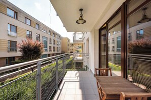 Un balcon avec une table et des chaises en bois, une rambarde en métal et une vue sur les immeubles voisins.
