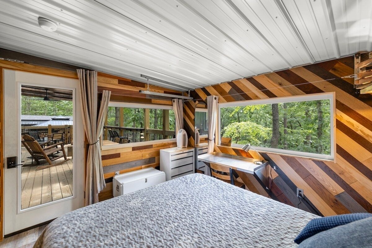 A bedroom with a large bed, a desk, and a view of the outdoors.