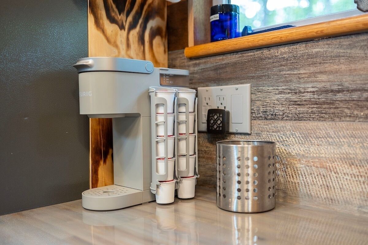 A coffee maker, a stack of disposable cups, and a metal container on a countertop.