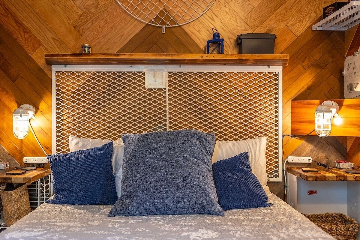Una camera da letto accogliente con soffitto in legno, un letto con biancheria azzurra e grigia e due lampade a parete.