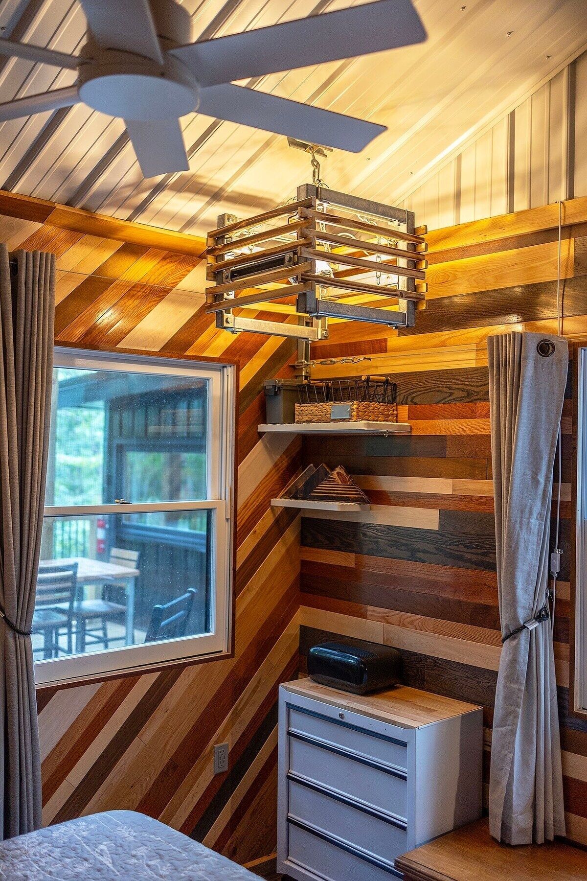 A bedroom with a sloped ceiling, a ceiling fan, a bed, a desk, and a window with curtains.