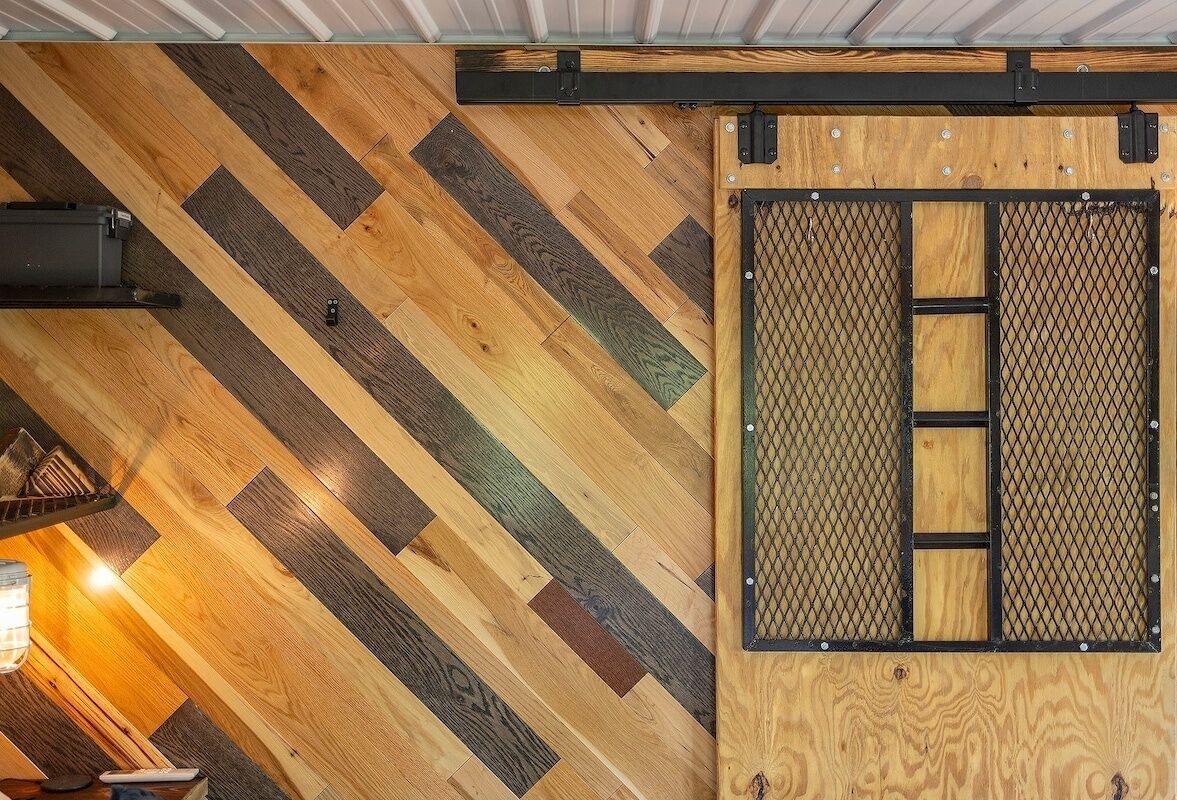 Une pièce dotée d’un parquet en bois à motifs en chevrons, d’une porte coulissante de style grange avec un moustiquaire, et d’un luminaire suspendu.