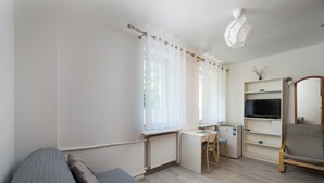 Une pièce comprenant un lit, un bureau, une chaise, un téléviseur et une étagère.