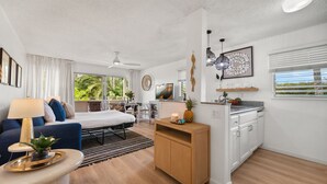 Een moderne, goed verlichte kamer met een bed, een slaapbank, een klein eethoekje en een keuken met witte kastjes.