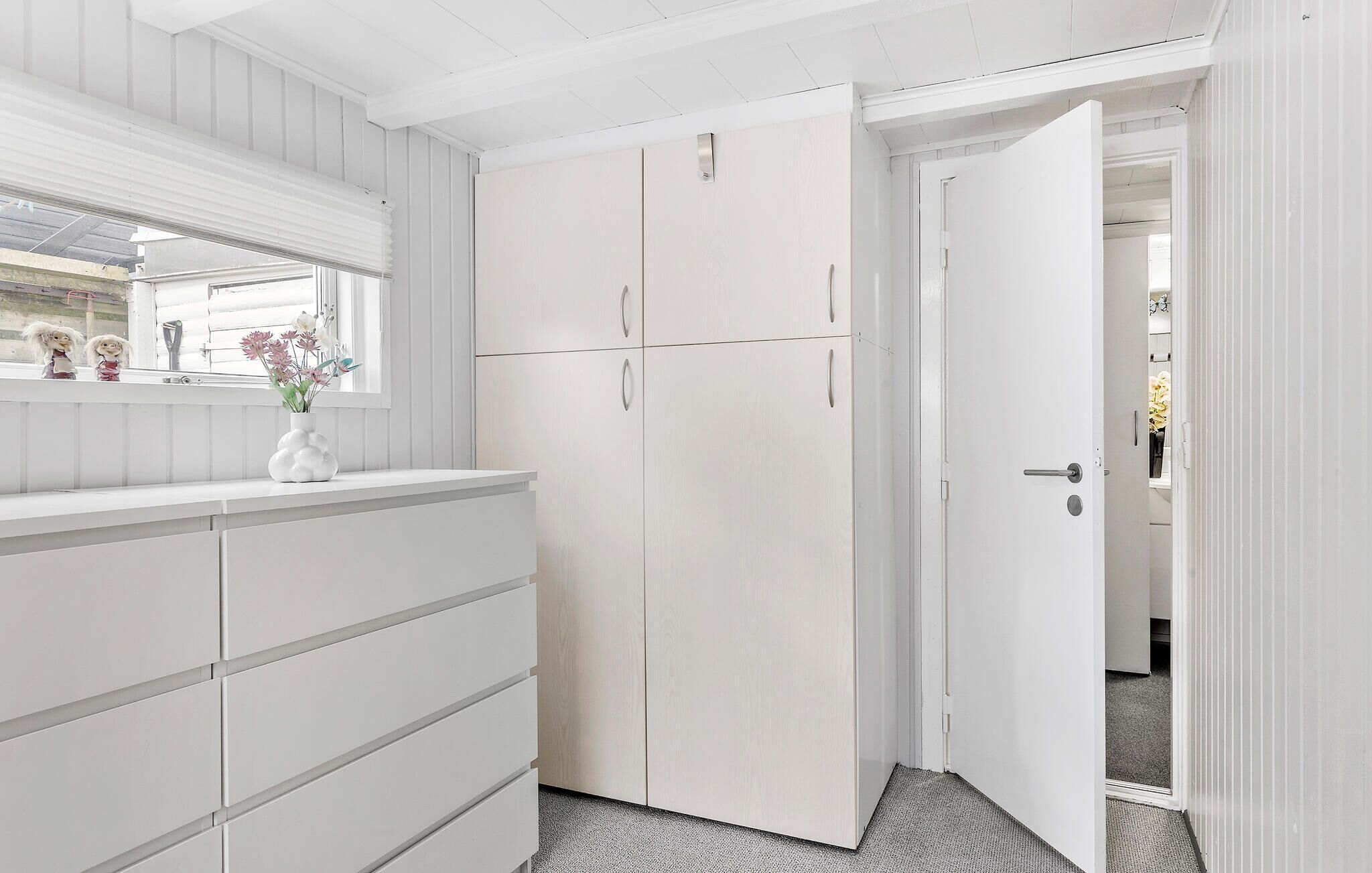 A white room with a large wardrobe, a dresser, and a mirror above the dresser.