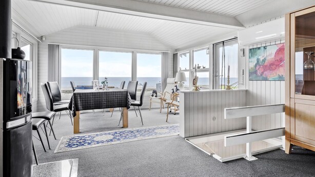 Une cuisine moderne dotée d’un grand îlot central, d’un coin repas offrant une vue sur la mer et d’un espace salon confortable avec une cheminée.