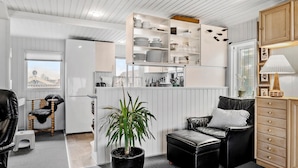 Un espace de vie compact comprenant un coin cuisine, un canapé en cuir noir, un meuble en bois et une plante en pot.