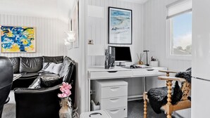 Une pièce moderne avec un bureau blanc, un canapé en cuir noir et une chaise en bois. Un tableau encadré est accroché au mur et un vase rempli de fleurs est posé sur le bureau.