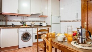 Cuina amb armaris blancs, una rentadora, una taula amb cadires i una cafetera.