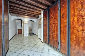 Un couloir doté d’un sol carrelé, de poutres en bois au plafond et d’une vue sur une pièce où se trouve un escalier.