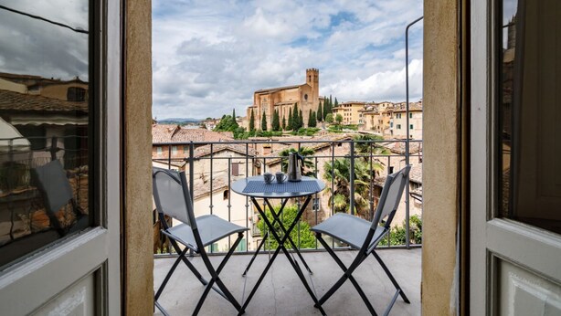 Un balcon avec deux chaises et une petite table, donnant sur un bâtiment historique doté d’une tour.