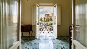 Une porte ouverte donnant sur un balcon d’où l’on peut admirer un bâtiment et des arbres.