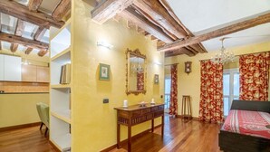 A room with wooden beams, a bed, a bedside table, a mirror, and a window with curtains.
