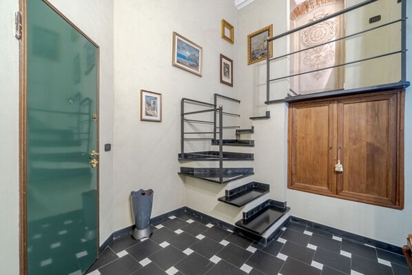 Una escalera con piso a cuadros blancos y negros, una puerta verde y un mueble de madera.