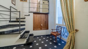 A staircase with black and white tiles, a wooden door, and a chair by a window with curtains.
