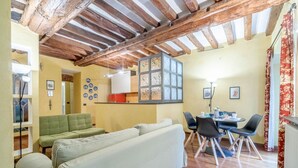 A cozy living area with a wooden ceiling, a sofa, a dining table with chairs, and a kitchen area with a red cabinet.