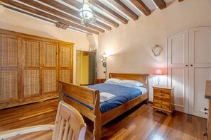 A bedroom with a wooden bed, a nightstand, a lamp, a wardrobe, and a chair.