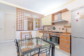 Una cocina moderna con una mesa de comedor de vidrio, armarios de madera y un refrigerador de acero inoxidable.