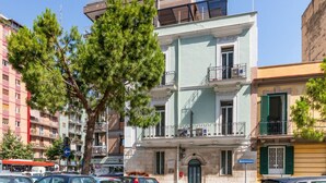 Un edificio de varios pisos con balcones, coches aparcados y cielo despejado.
