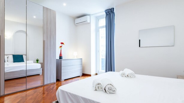 Habitación de hotel con cama, tocador, espejo y ventana con cortinas.
