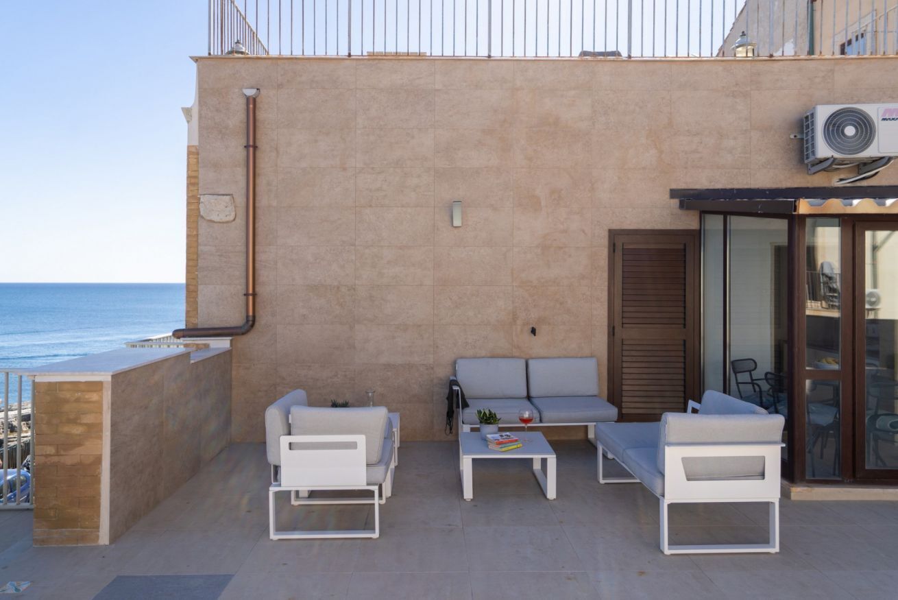 A balcony with white furniture, a small table, and a view of the sea.