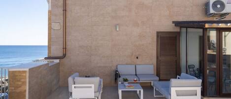 A balcony with white furniture, a small table, and a view of the sea.