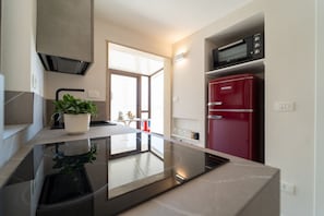 A modern kitchen with a built-in stove, a red refrigerator, and a potted plant on the counter. - GuestHost - Elegant 115 sqm apartment, for 4 people, located in the historic center (Traffic-Restricted Area), facing the Vittorini seafront and from which it is possible to access the main tourist attractions of the city on foot.The accommodation, insid (Siracusa)