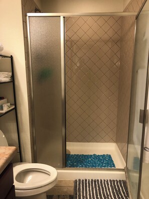 A shower with a glass door, a white toilet, and a shelf with towels. - Charming 2-bedroom basement Apartment with AC and WiFi in terrific Aurora (Aurora)