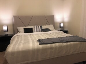 A neatly made bed with a striped bedspread, two bedside tables with lamps, and a headboard. - Charming 2-bedroom basement Apartment with AC and WiFi in terrific Aurora (Aurora)