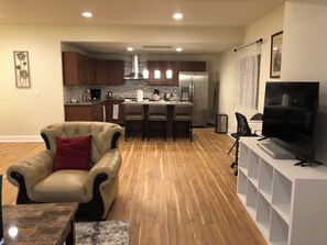 A modern living room with a leather armchair, a dining area with a kitchen in the background, and a TV on a stand. - Charming 2-bedroom basement Apartment with AC and WiFi in terrific Aurora (Aurora)