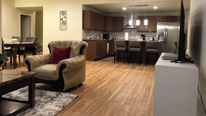 Een moderne woonkamer met een leren bank, een eettafel en een keuken met houten kasten en een roestvrijstalen koelkast.