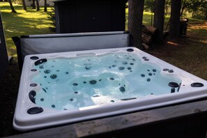 Un bain à remous doté de plusieurs jets, entouré d’une terrasse en bois et d’arbres.