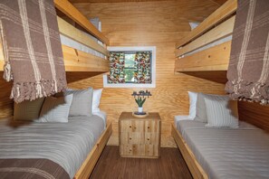 Une chambre confortable, aménagée dans le style d’un chalet, avec deux lits superposés, une petite table de chevet en bois ornée d’une plante et une fenêtre avec des rideaux.