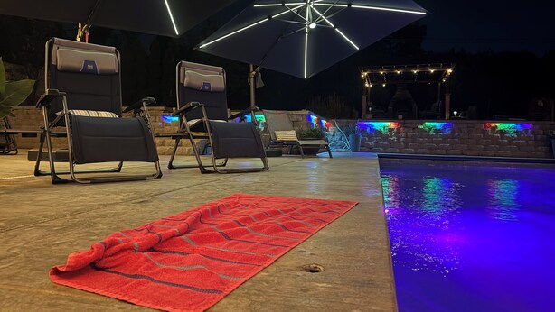 A poolside area with lounge chairs, a red towel, and a pool with colorful LED lights. - Desert Oasis with in ground pool, 4 bedrooms, 3 baths in the heart of Yakima! (Yakima)