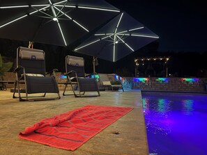A poolside area with lounge chairs, a red towel, and a pool with colorful LED lights. - Desert Oasis with in ground pool, 4 bedrooms, 3 baths in the heart of Yakima! (Yakima)