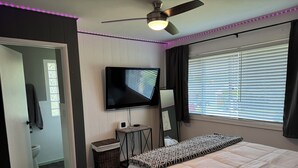 A bedroom with a bed, a TV, a ceiling fan, a window with blinds, and a door leading to a bathroom. - Desert Oasis with in ground pool, 4 bedrooms, 3 baths in the heart of Yakima! (Yakima)