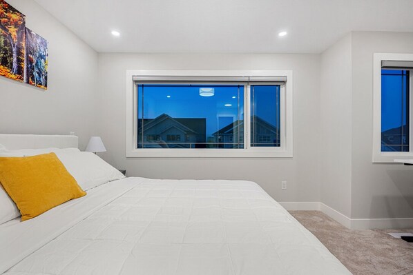 Une chambre avec un grand lit, une fenêtre donnant sur des maisons et un tableau accroché au mur.